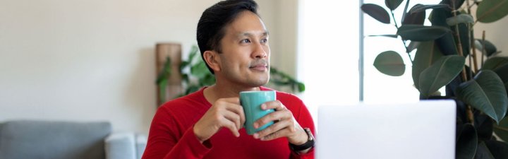 A man holding a mug with both hands is smiling and looking out into the distance